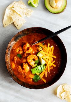 a bowl filled with shrimp, cheese and tortilla chips next to an avocado