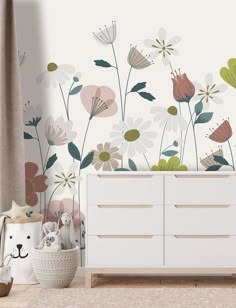 a white dresser sitting next to a wall with flowers on it