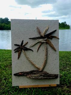 a piece of art made out of driftwood sitting on top of grass next to a body of water