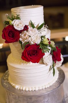 a three tiered cake with red and white flowers on the top is sitting on a silver platter