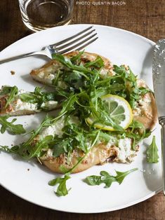 a white plate topped with pizza covered in greens next to a fork and glass of water