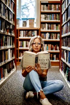 a woman sitting on the floor reading a book in a library with many bookshelves