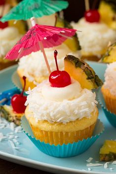 some cupcakes with fruit on top and an umbrella in the middle are sitting on a blue plate