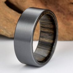 a wedding band with wood inlaying the center on a white table next to a piece of wood