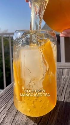 a person pouring cold beverage into a mason jar with ice and orange juice in it