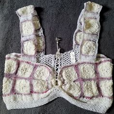 a white crocheted sweater laying on top of a gray floor next to a button