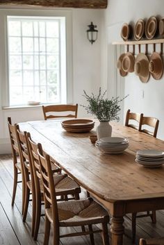 a wooden table with plates and bowls on it in a white walled dining room area