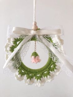 a crocheted wreath hanging from a white ribbon with a pink flower on it