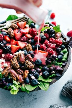 someone pouring dressing onto a salad with berries and blueberries