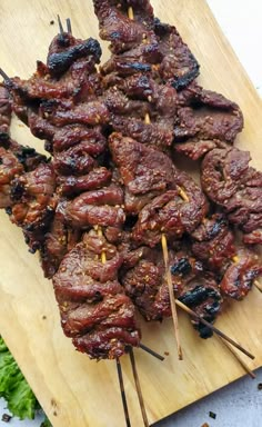 several skewers of meat sitting on top of a wooden cutting board