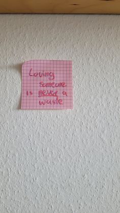 a piece of pink paper with writing on it sitting on top of a white wall