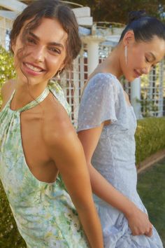 two young women standing next to each other in front of a white fence and bushes