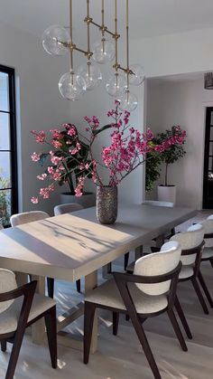 a dining room table with chairs and a vase filled with pink flowers on top of it