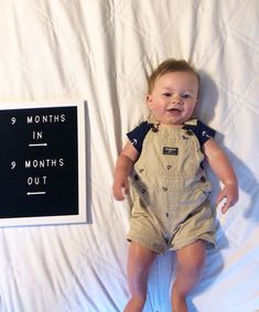 a baby laying on top of a bed next to a sign that says months in 9 months out