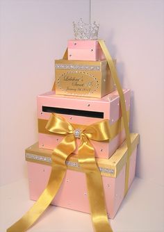 three pink boxes stacked on top of each other with gold ribbons around them and a tiara hanging from the top