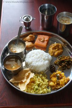 a metal plate topped with rice and different types of food on top of a wooden table