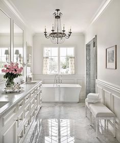 a white bathroom with chandelier, tub and sink in the middle of it