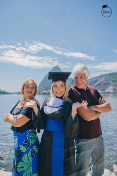 an older man and two women in graduation gowns posing for a photo by the water