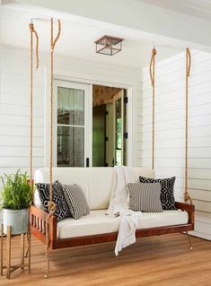 a porch swing with pillows on it and a potted plant next to it in front of the door