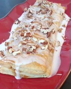 a red plate topped with a pastry covered in icing and nuts