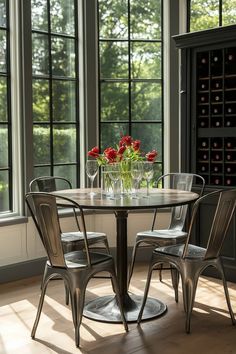 a glass table with four chairs around it in front of two wine bottles and windows