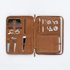 an open brown leather case with various items in it on a white surface, top view