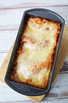 a casserole dish with meat and cheese in it sitting on a wooden cutting board