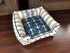 a dog bed on the floor with an anchor and stripe pattern, that says bear