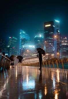 two people with umbrellas standing on the sidewalk in front of city buildings at night