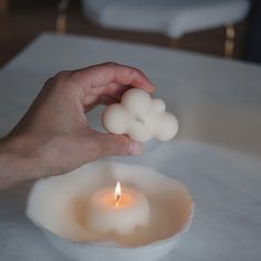 a person holding a candle in front of a white plate with a cloud on it