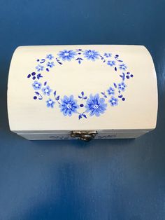 a white box with blue flowers painted on the front and sides, sitting against a blue background