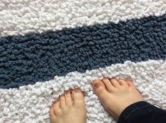 a person standing on top of a white and blue crocheted blanket next to a persons feet