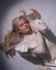 a woman with long blonde hair laying on the ground wearing a white dress and holding her hands to her face