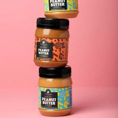 three jars of peanut butter stacked on top of each other in front of a pink background