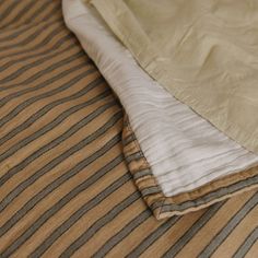 an unmade bed with brown and white sheets on it's side, next to a striped comforter