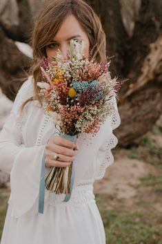 a woman wearing a white dress holding a bouquet of wildflowers in her hands