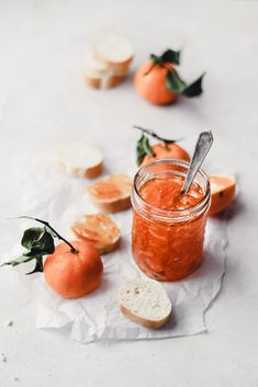 an orange jam in a glass jar surrounded by slices of bread and tangerines