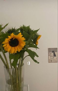 a vase filled with yellow sunflowers on top of a wooden table next to a white wall