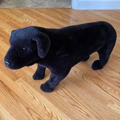 a black stuffed dog standing on top of a hard wood floor