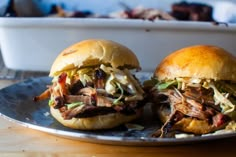 two pulled pork sandwiches sitting on top of a metal plate next to a white container