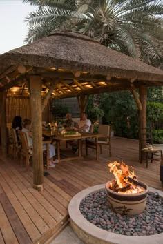 people sitting around a fire pit on a wooden deck with palm trees in the background