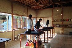 two people standing in a room with lots of shoes on the floor and one person sitting at a table