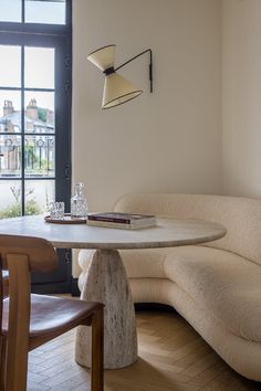 a corner table with a book on it in front of a window and some chairs