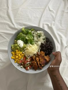 a person holding a bowl full of food on top of a white sheet covered table