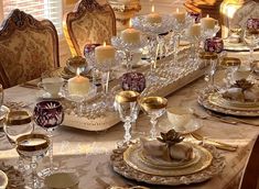 a dining room table is set with gold and white dishes, candles, and china