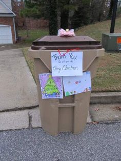 a trash can with a note attached to it on the side of the road next to a mailbox