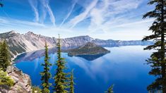 a lake surrounded by trees and mountains under a blue sky with wispy clouds