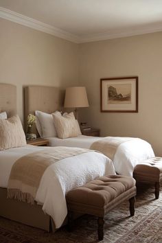 two beds in a hotel room with white linens and tan bedding, one has a footstool