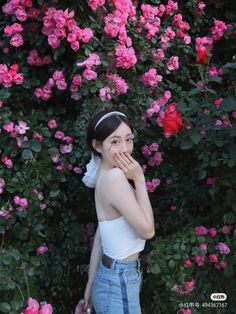 a woman standing in front of pink flowers with her hand on her face and looking at the camera