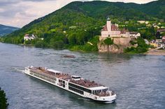 a large white boat traveling down a river next to a lush green hillside